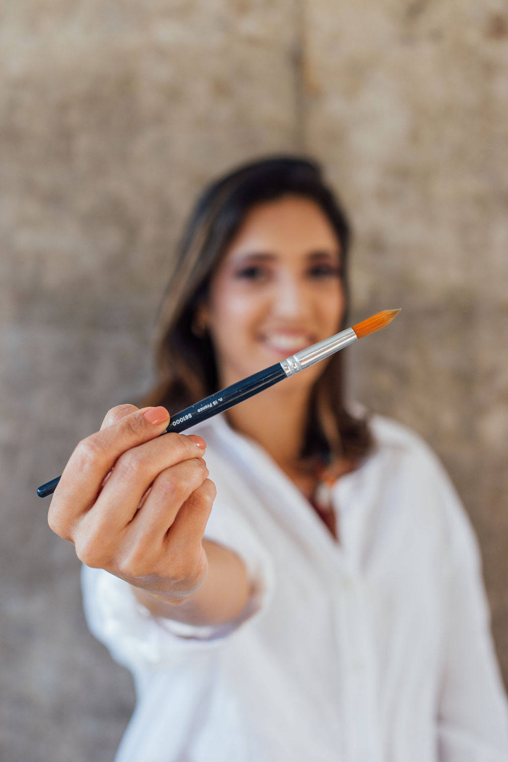 Maisa Cardoso sorrindo, segurando um pincel de pintura voltado para a câmera